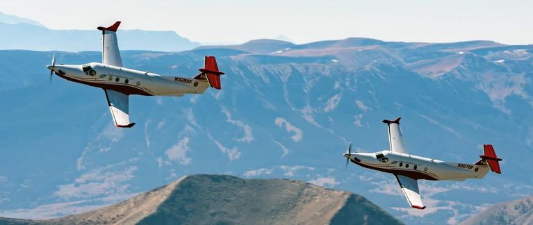 Two Pilatus PC 12 Multi-mission aircraft flying over mountains